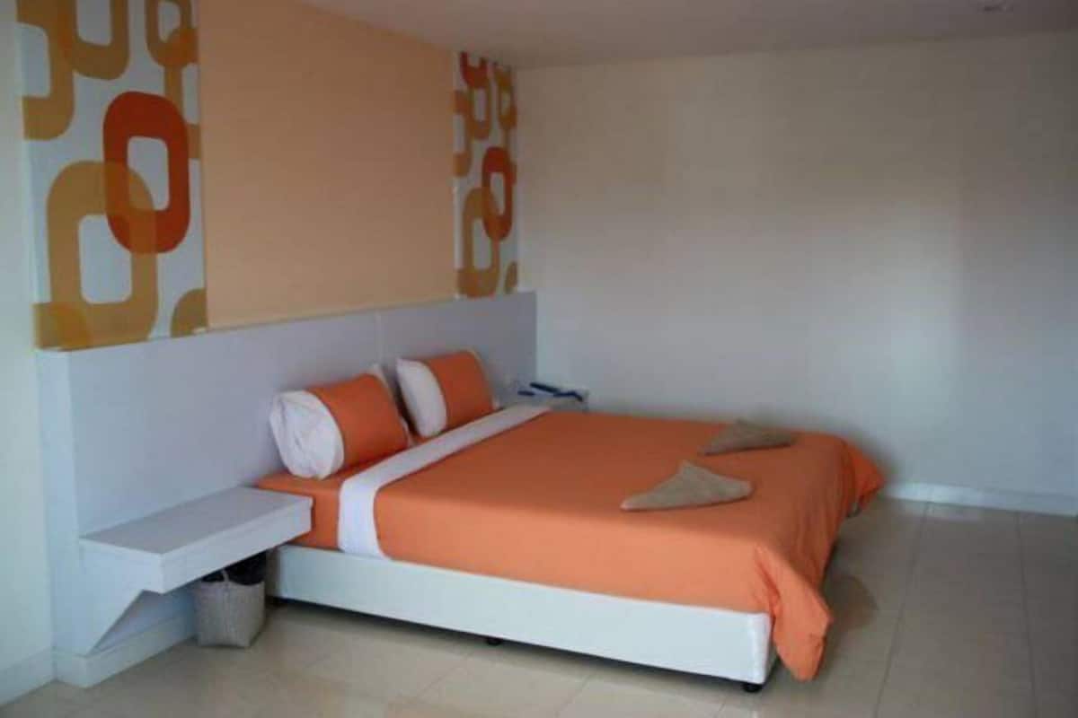Quarto com cama branca, roupa de cama laranja e mesa de cabeceira branca.
