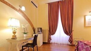 Una habitación con un escritorio de madera, una silla, una lámpara, una planta en maceta, un televisor y una cama con un edredón estampado.