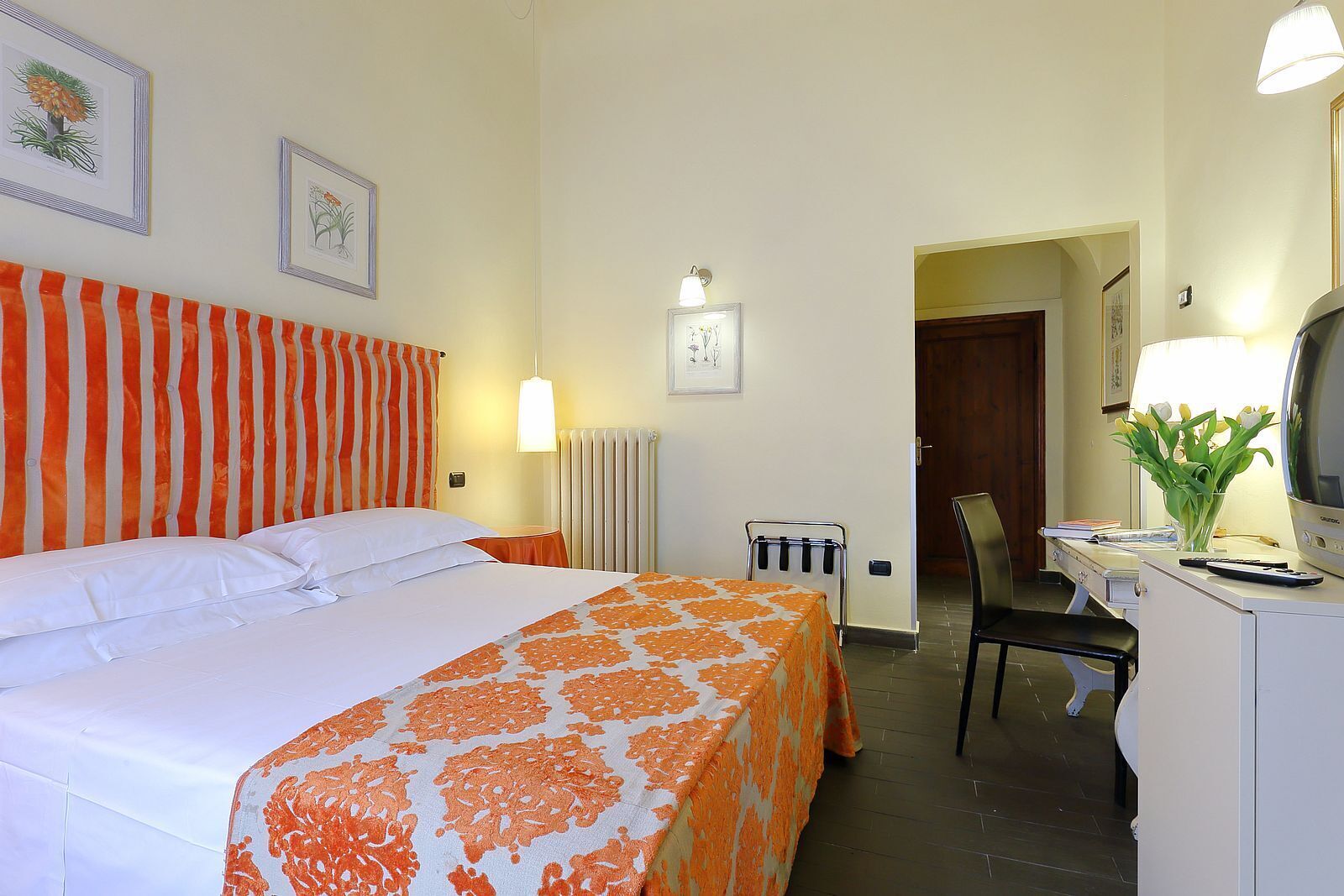 A hotel room with a bed, a desk with a chair, a radiator, and a television.