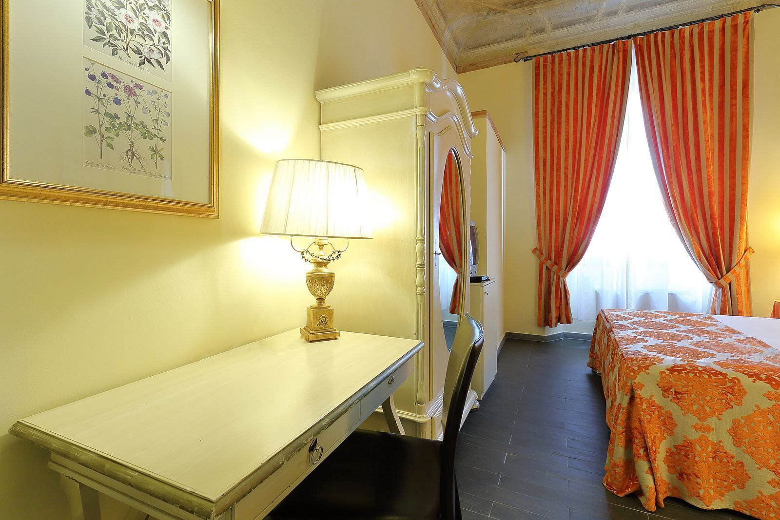 Ein Hotelzimmer mit Bett, Schreibtisch, Lampe und einem fensterbepflanzten Fenster.