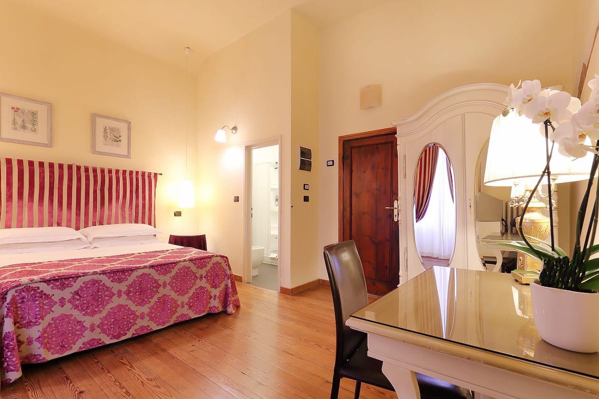 A hotel room with a bed, a desk, a chair, a mirror, and a bathroom visible through an open door.