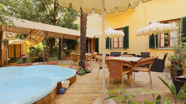 Una terraza de madera con un jacuzzi, mobiliario exterior y sombrillas.