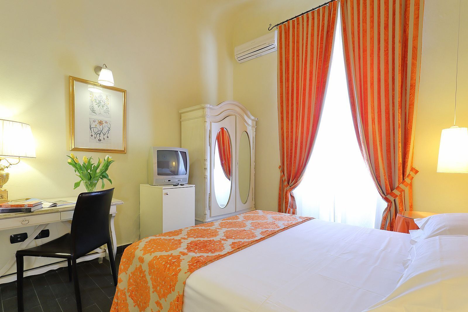 A hotel room with a bed, desk, chair, television, mirror, and curtains.