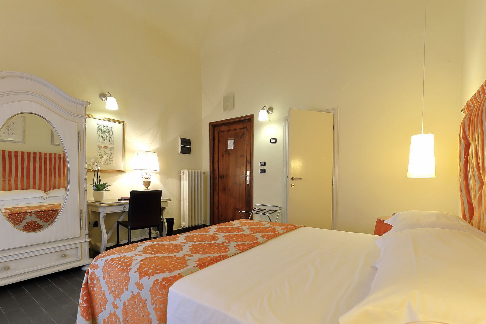 A hotel room with a bed, a desk, a chair, a mirror, and a door.