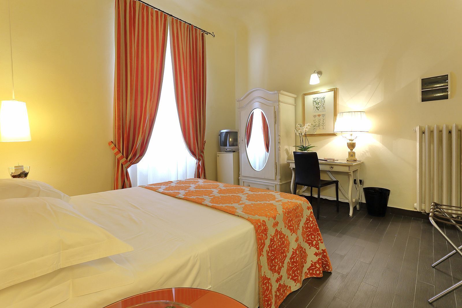 Une chambre d’hôtel comprenant un lit, un bureau avec une chaise, un miroir, une lampe et un radiateur.