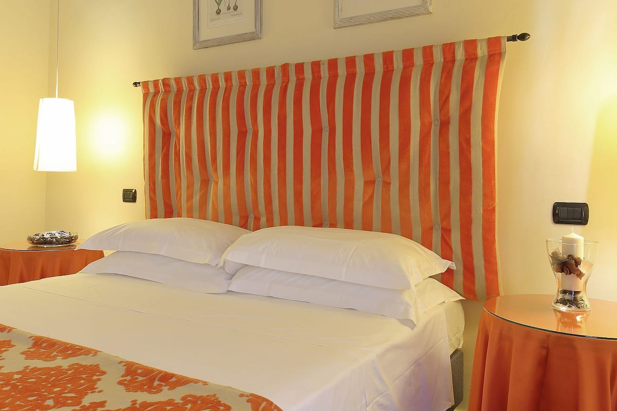 A hotel room with a bed, striped curtains, a bedside table with a candle, and a wall-mounted light switch.