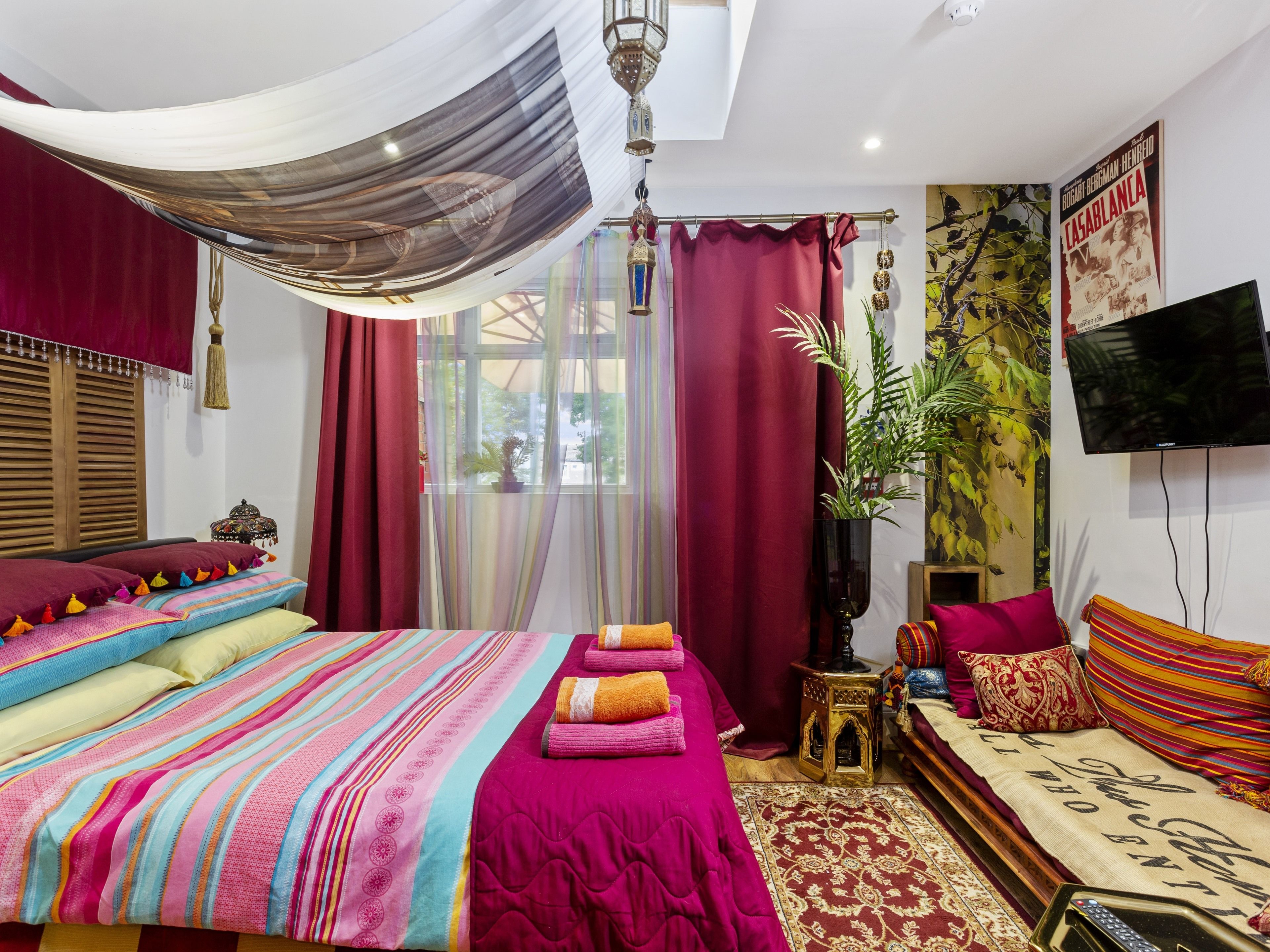 A well-lit bedroom with a large bed, a sofa, a TV, and a window with curtains.