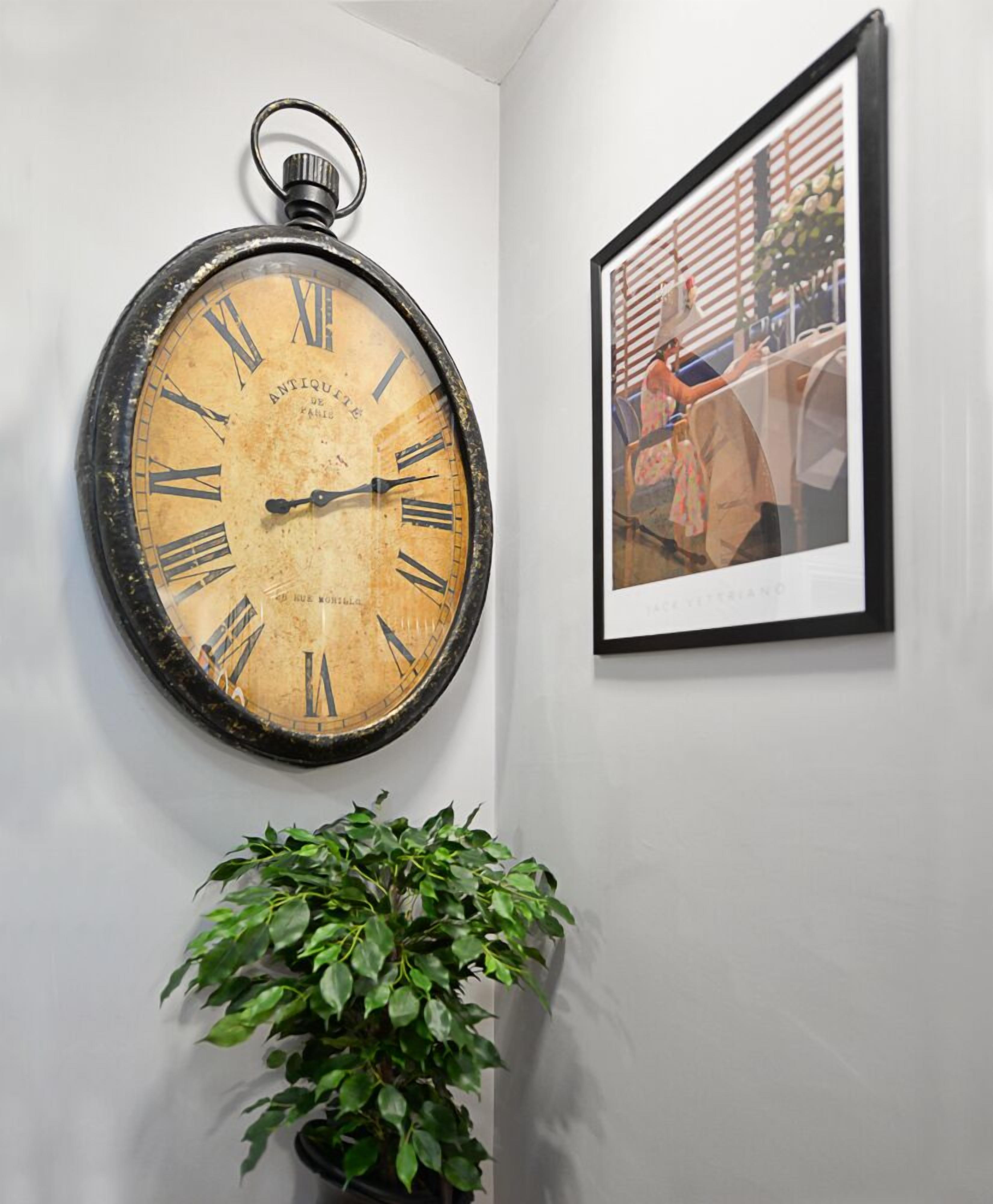 Eine wandmontierte Taschenuhr mit römischen Ziffern, ein gerahmtes Foto und ein Blumentopf.