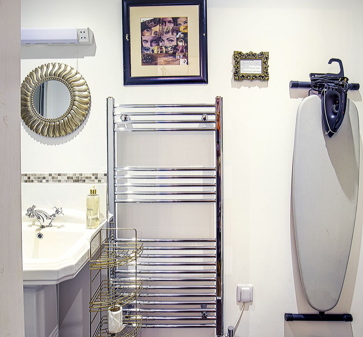 A bathroom with a chrome towel rack, a sink with a mirror, a framed artwork, and a toilet.