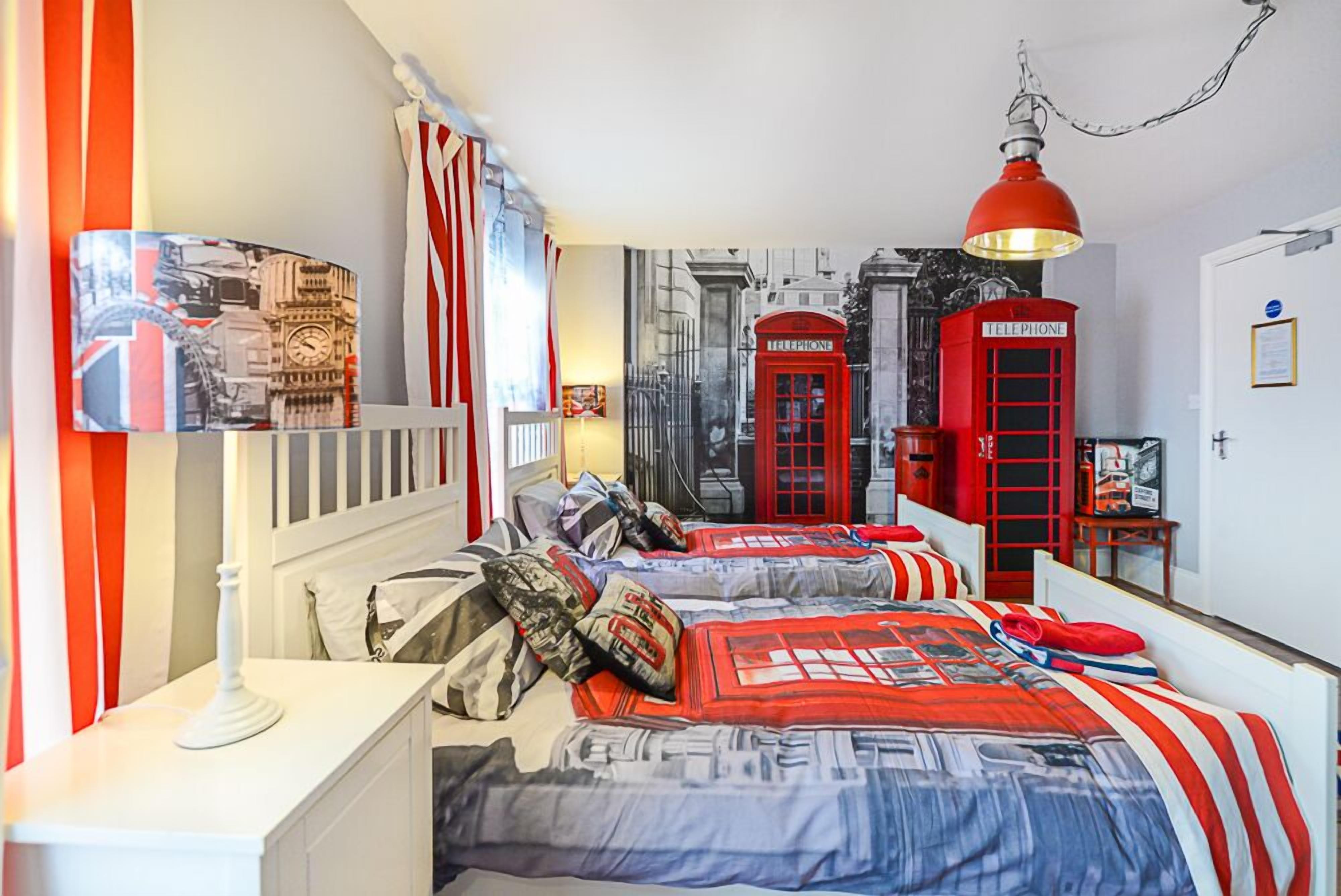 Una habitación con dos camas, cabinas telefónicas rojas y una lámpara.