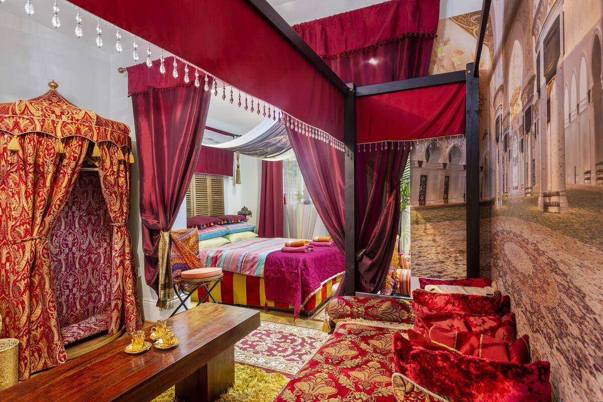 A room with a canopy bed, a wooden bench, and a red carpet.