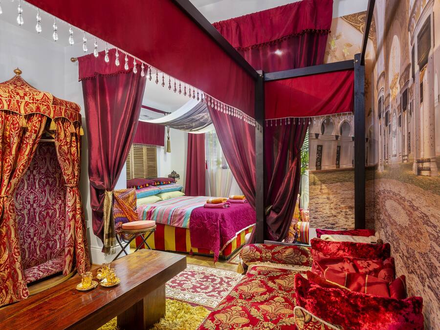 Une chambre avec un lit à baldaquin, un banc en bois et une moquette rouge.