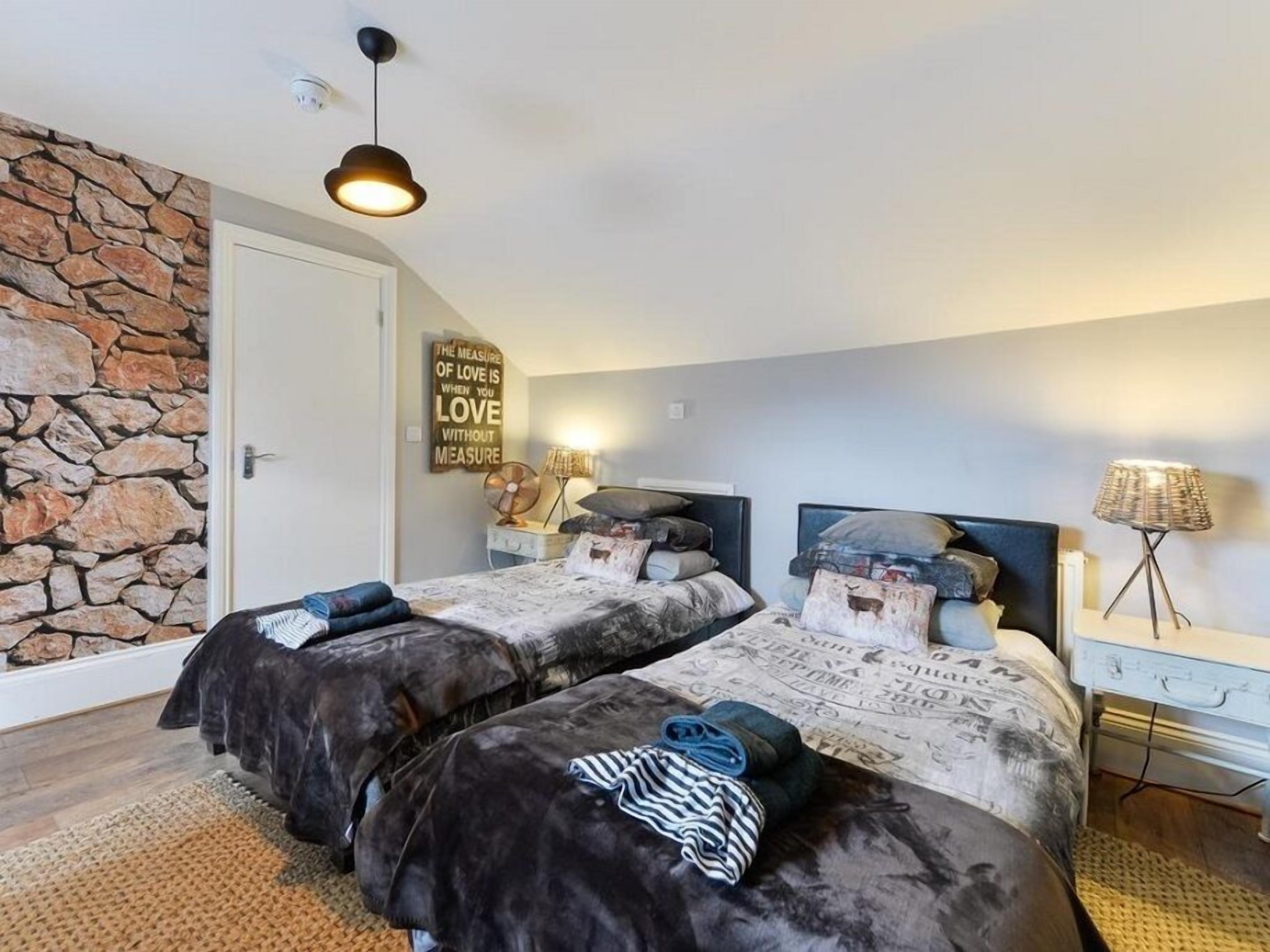 A bedroom with two beds, a stone wall, a ceiling fan, and a motivational quote on the wall.
