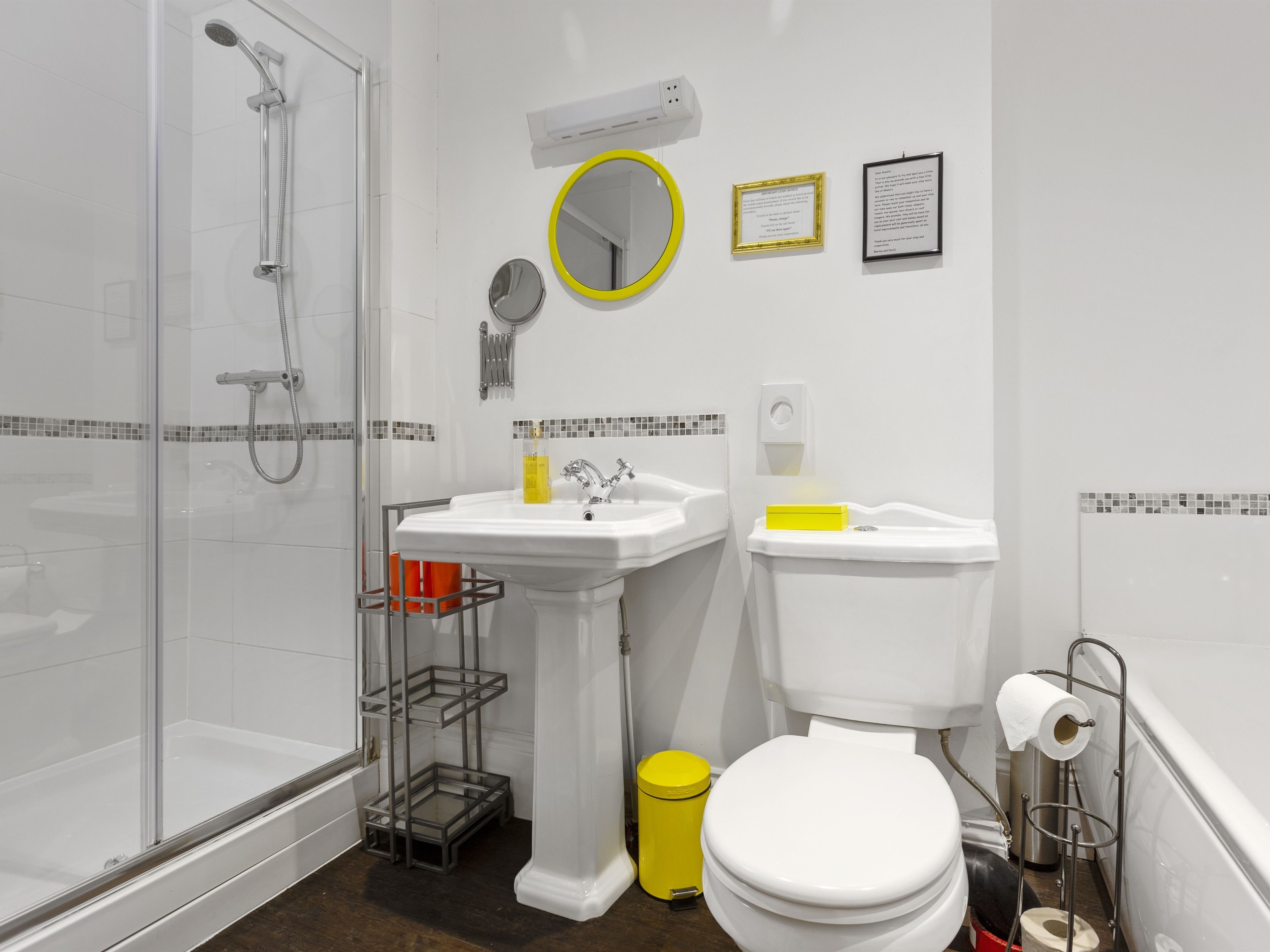 Een moderne badkamer met een glazen douchecabine, een wastafel op een zuil, een toilet en een kleine prullenbak.