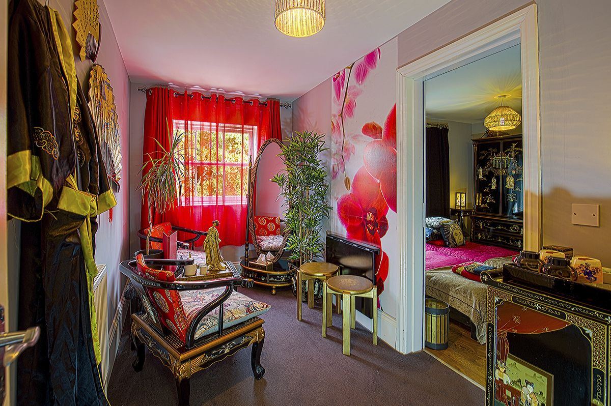 A room with a bed, a small table, a chair, a radiator, and a mirror.
