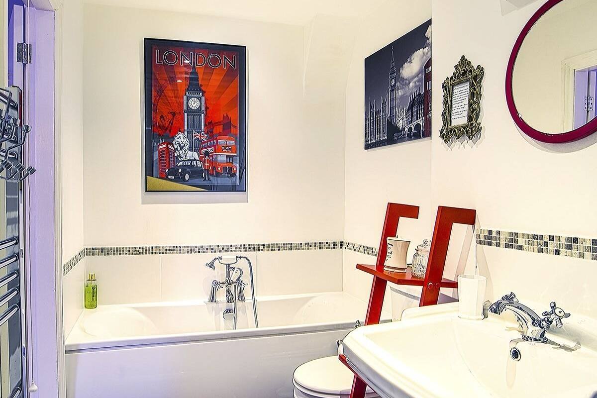 A bathroom with a bathtub, a sink, and a toilet. There are two framed pictures on the wall, one of London and another of a building.