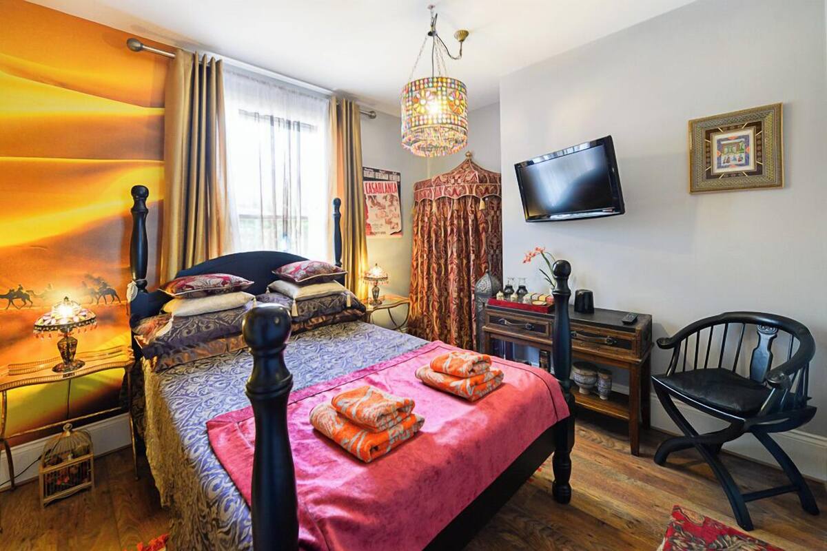 A bedroom with a bed, a TV, a chair, a desk, and a chandelier.