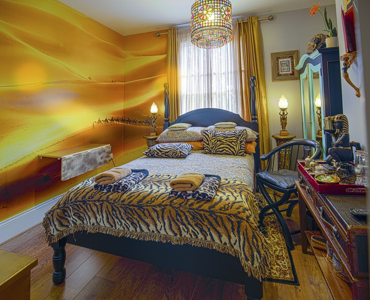 A bedroom with a bed, a chair, a dresser, a mirror, and a chandelier.