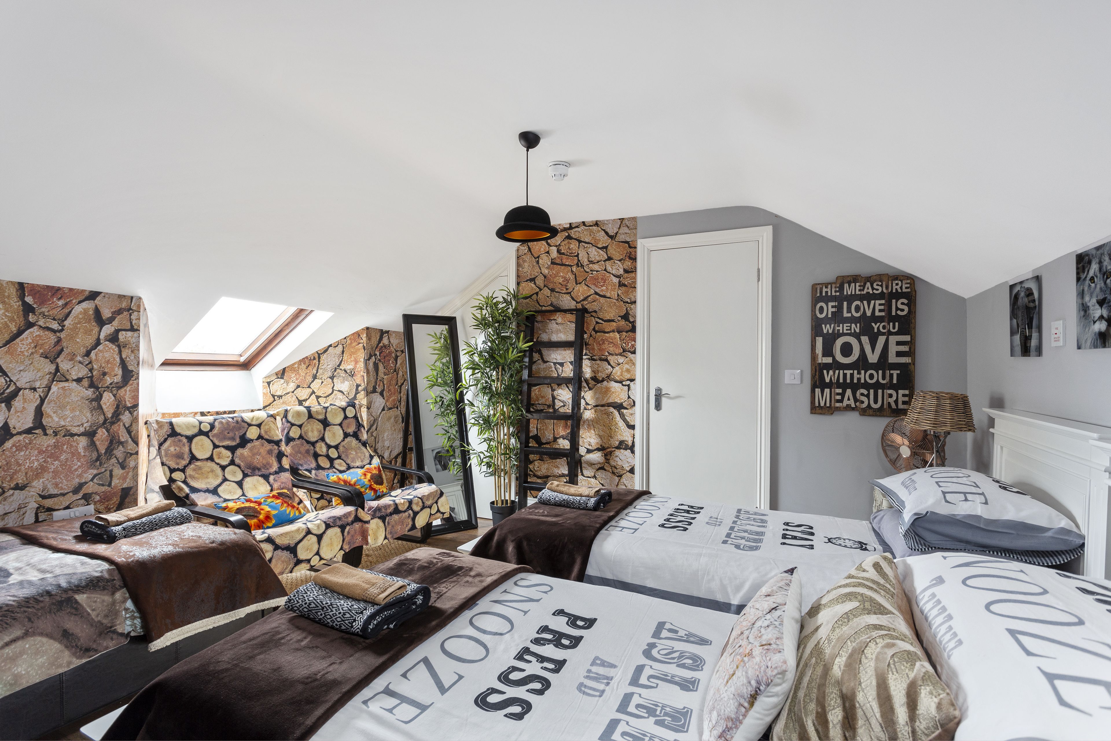 A room with two beds, a stone wall, a skylight, and a motivational quote on the wall.