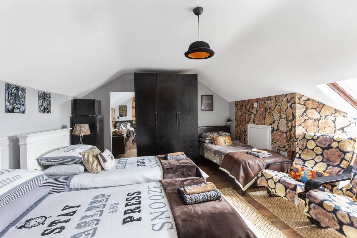 A bedroom with two beds, a sofa, a chair, and a stone-patterned wall.