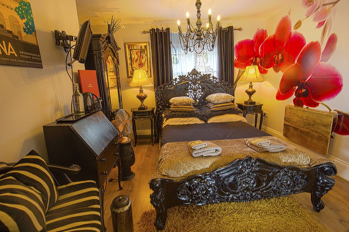 Une chambre traditionnelle avec un grand lit, un bureau, une chaise, un lustre et une orchidée rouge.