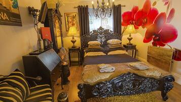 Una habitación tradicional con una cama grande, un escritorio, una silla, una araña y una orquídea roja.