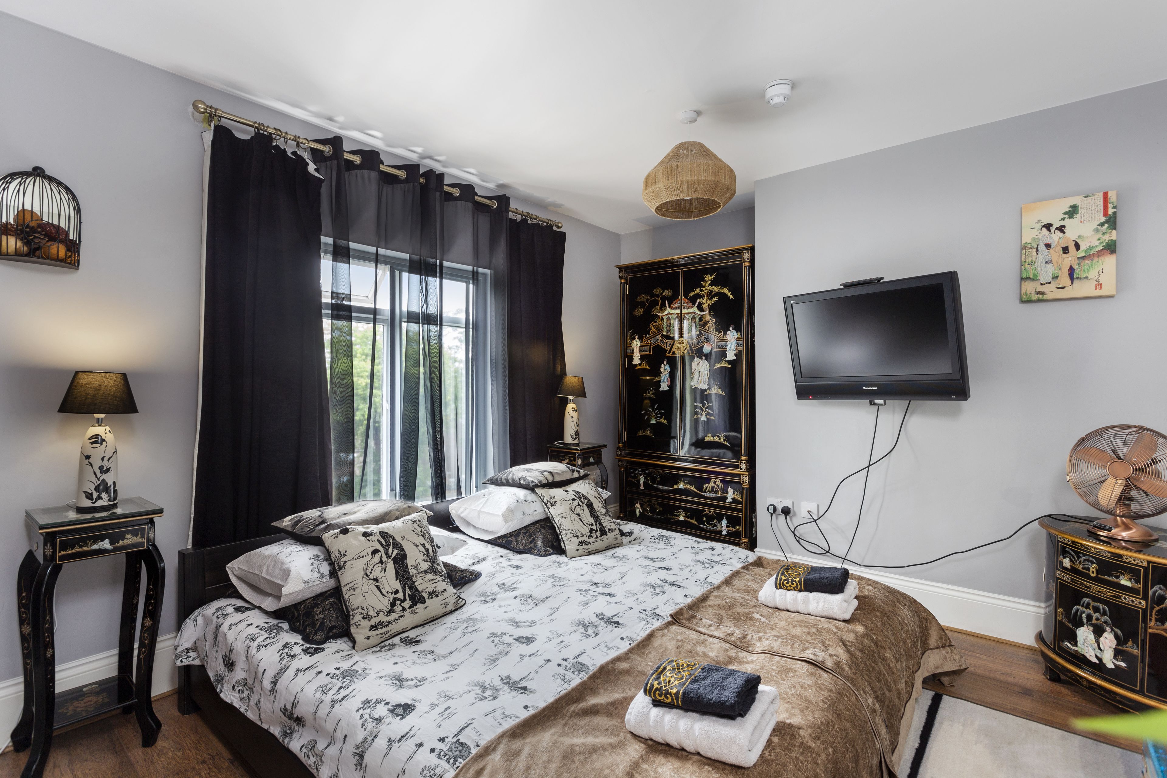 Un dormitorio con una cama grande, televisor, cómoda y ventana con cortinas.