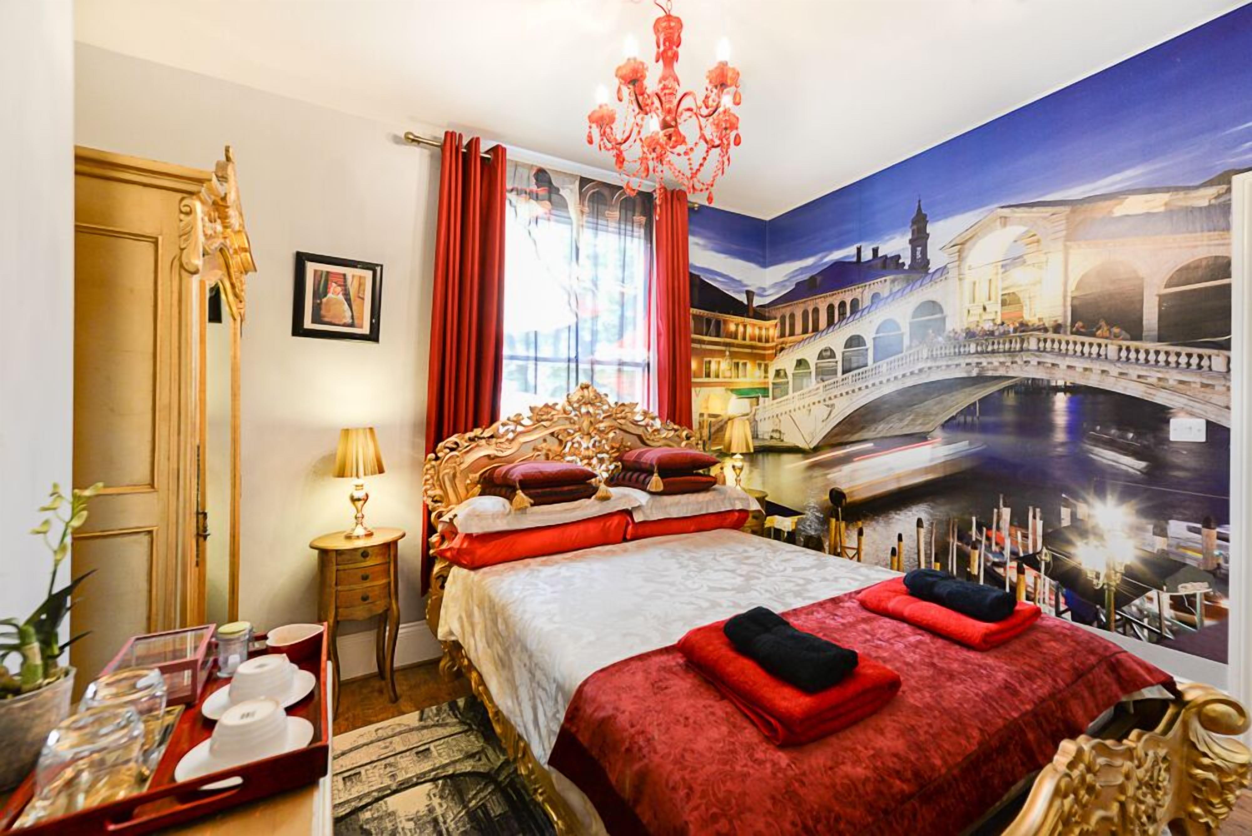 A luxurious bedroom with a large bed, ornate headboard, and a mural of a bridge.