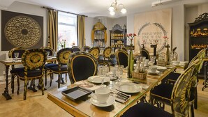 A dining area with ornate chairs, a long table set for a meal, and a decorative wall with a quote. - Mama's Inn Boutique Guest House (Nottingham)