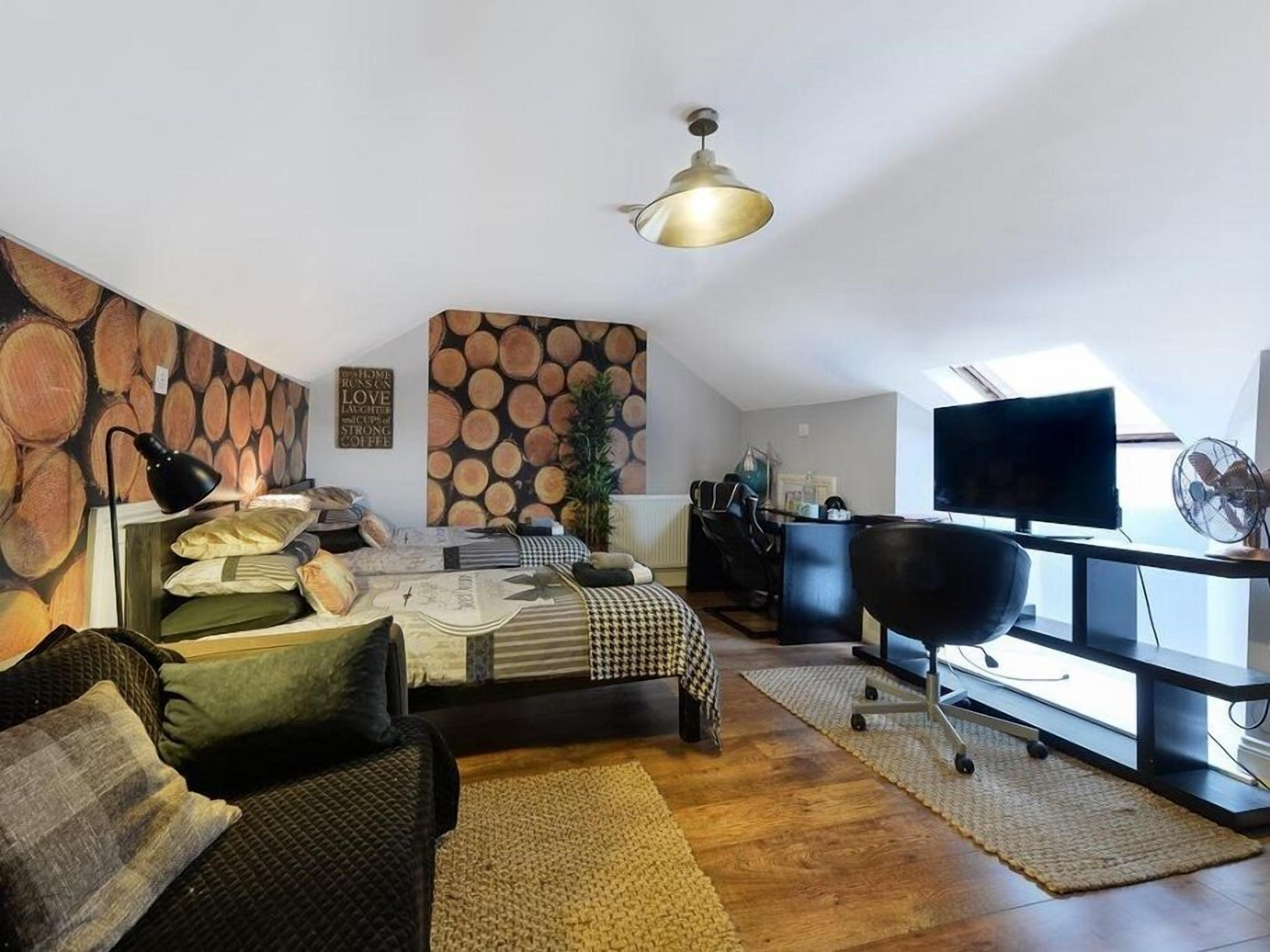 Un salon moderne comprenant un canapé, une table basse, un téléviseur et un mur décoré d’un motif imitant des troncs d’arbres.