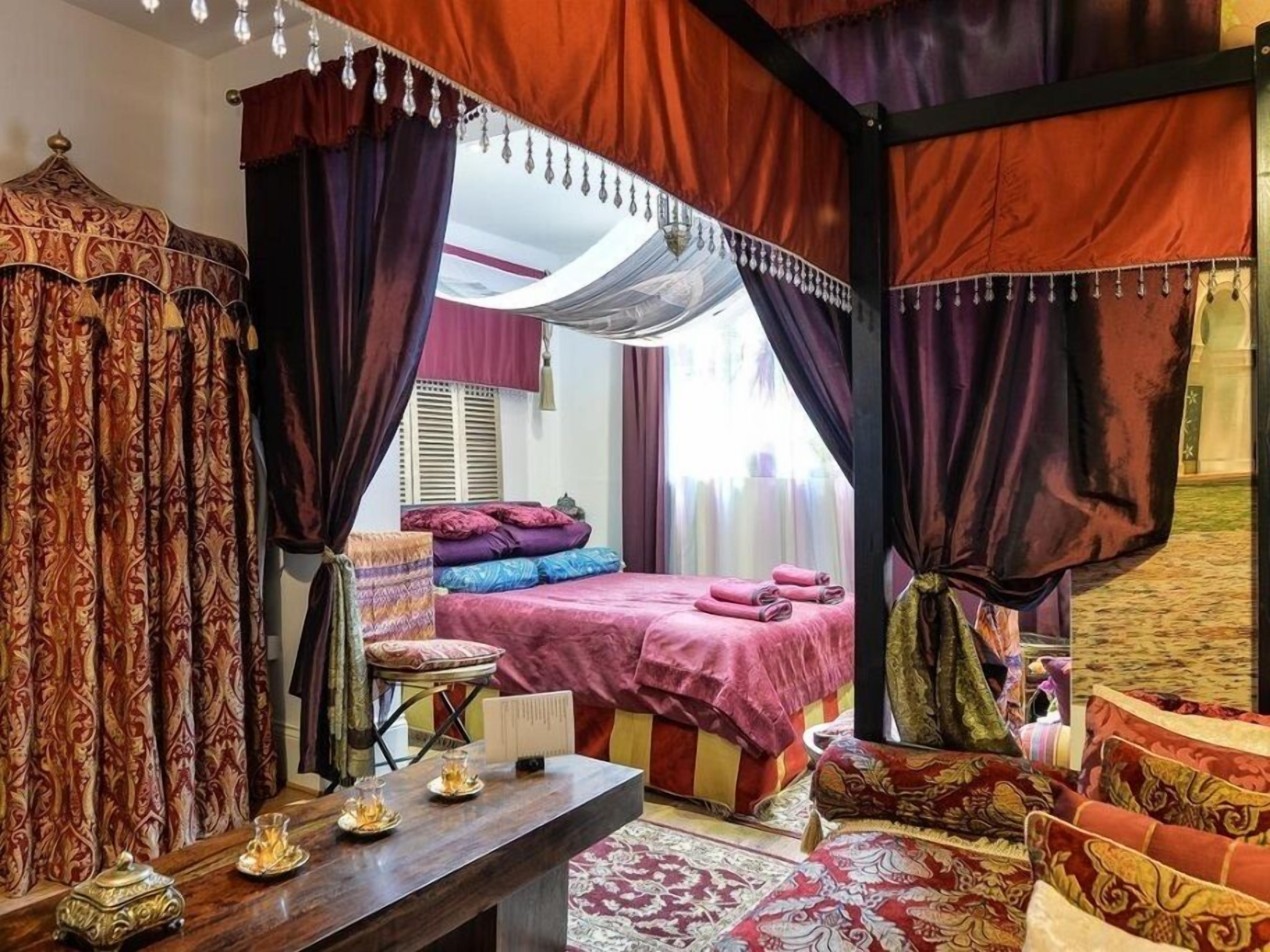 Una cama con dosel y cuatro columnas, una mesita de noche con lámpara, y vista de la habitación.