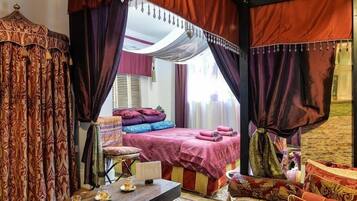 Una cama con dosel y cuatro columnas, una mesita de noche con lámpara, y vista de la habitación.