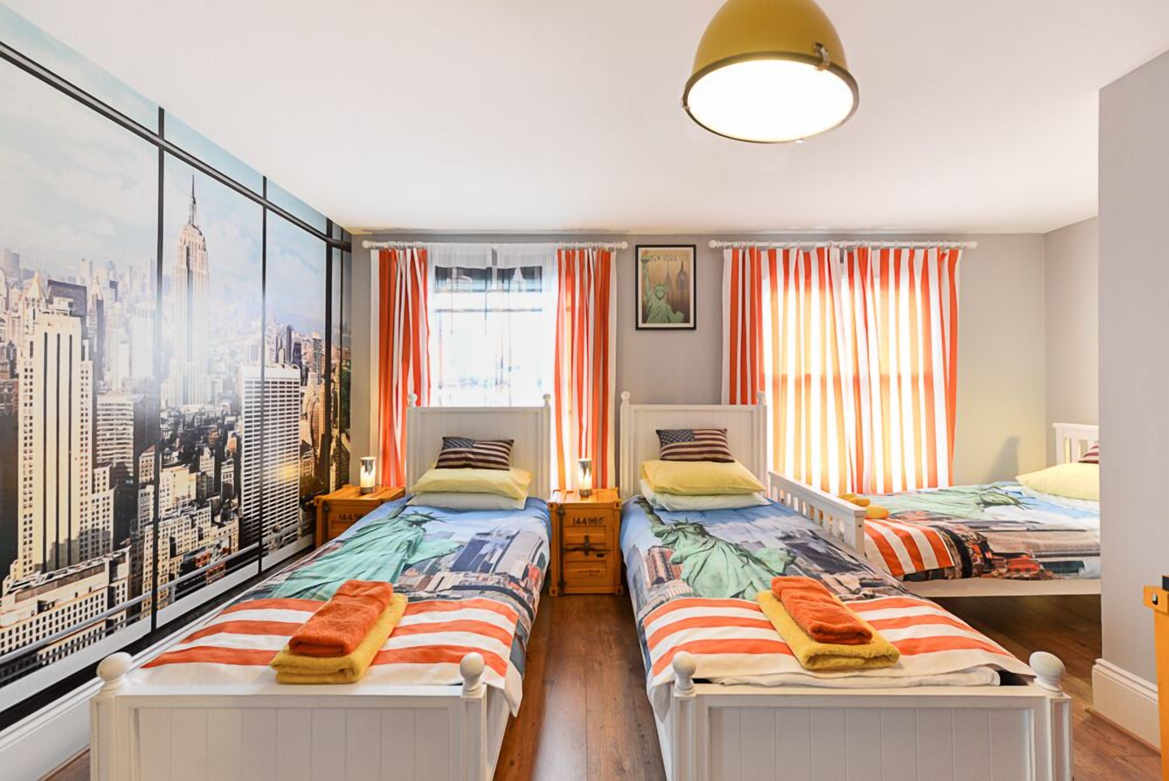 A hotel room with two beds, striped curtains, a cityscape mural, and a large window.