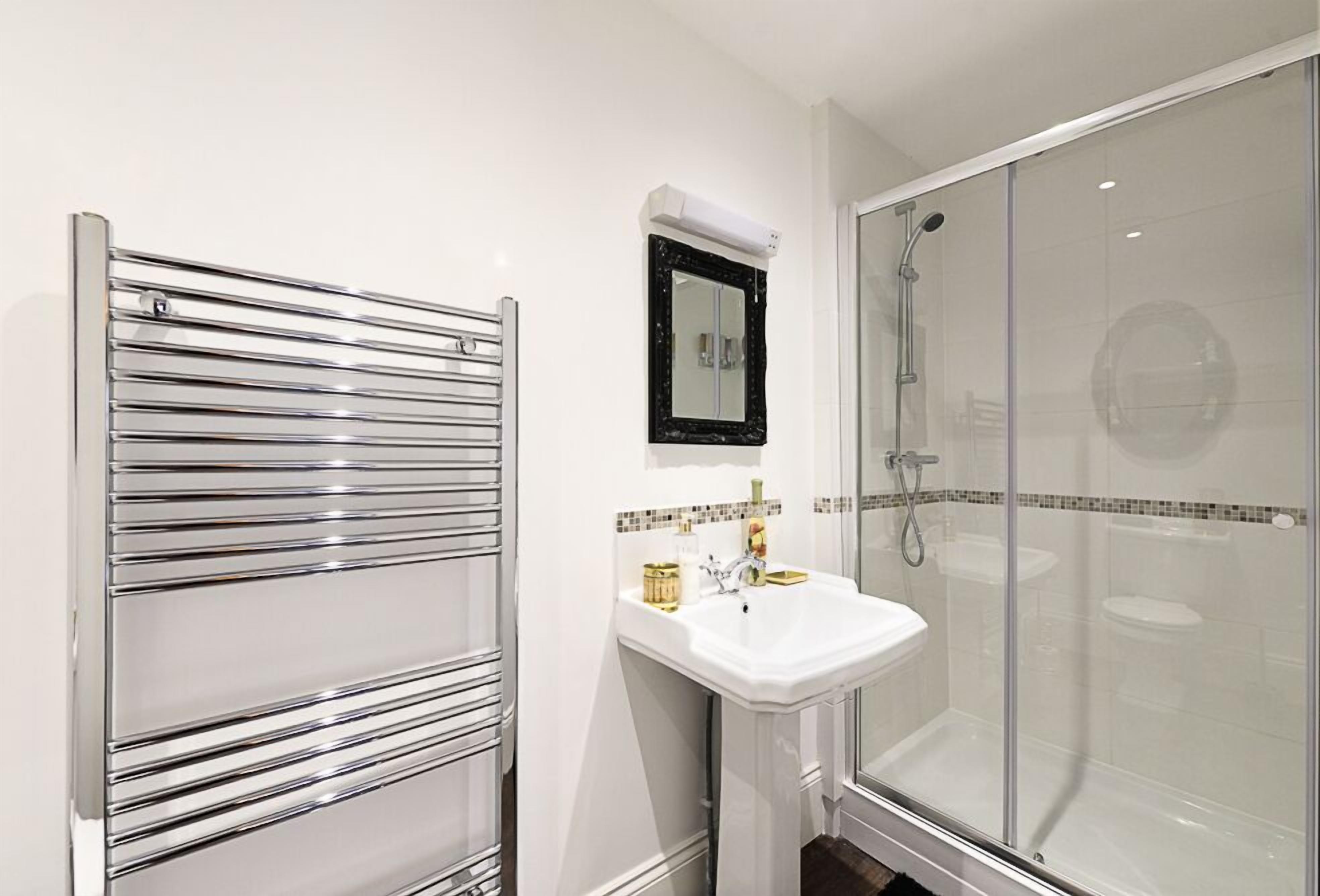 A modern bathroom with a chrome towel rack, a white sink with a mirror above it, and a glass-enclosed shower area.