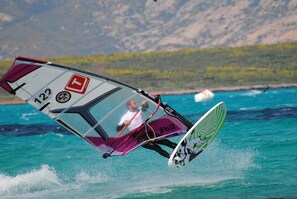 A person windsurfing on turquoise water with a mountainous backdrop. - Hotel Ristorante Silvestrino (Stintino)