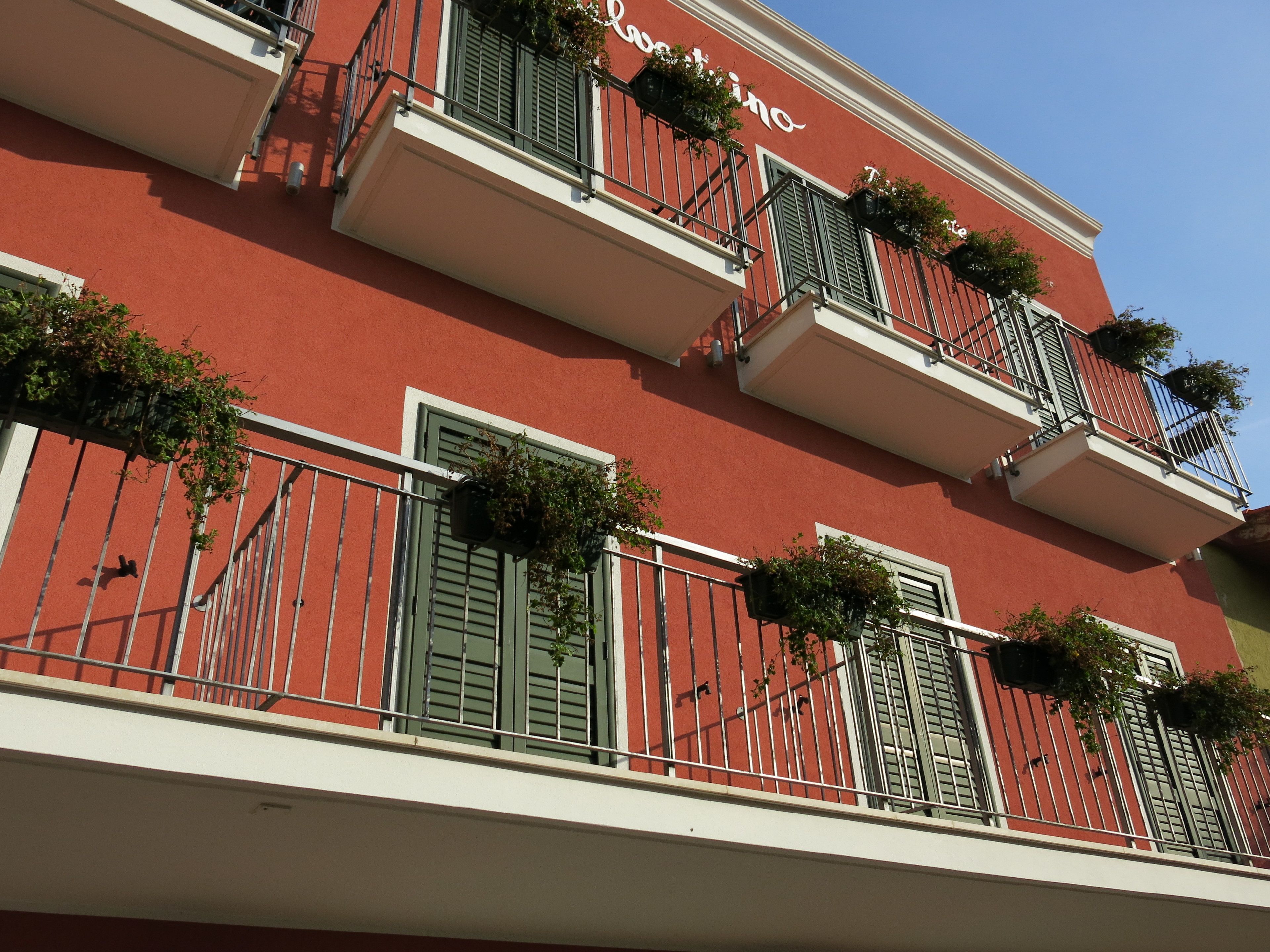 Een rood gebouw met meerdere balkons, elk voorzien van groene luiken en bloempotten.