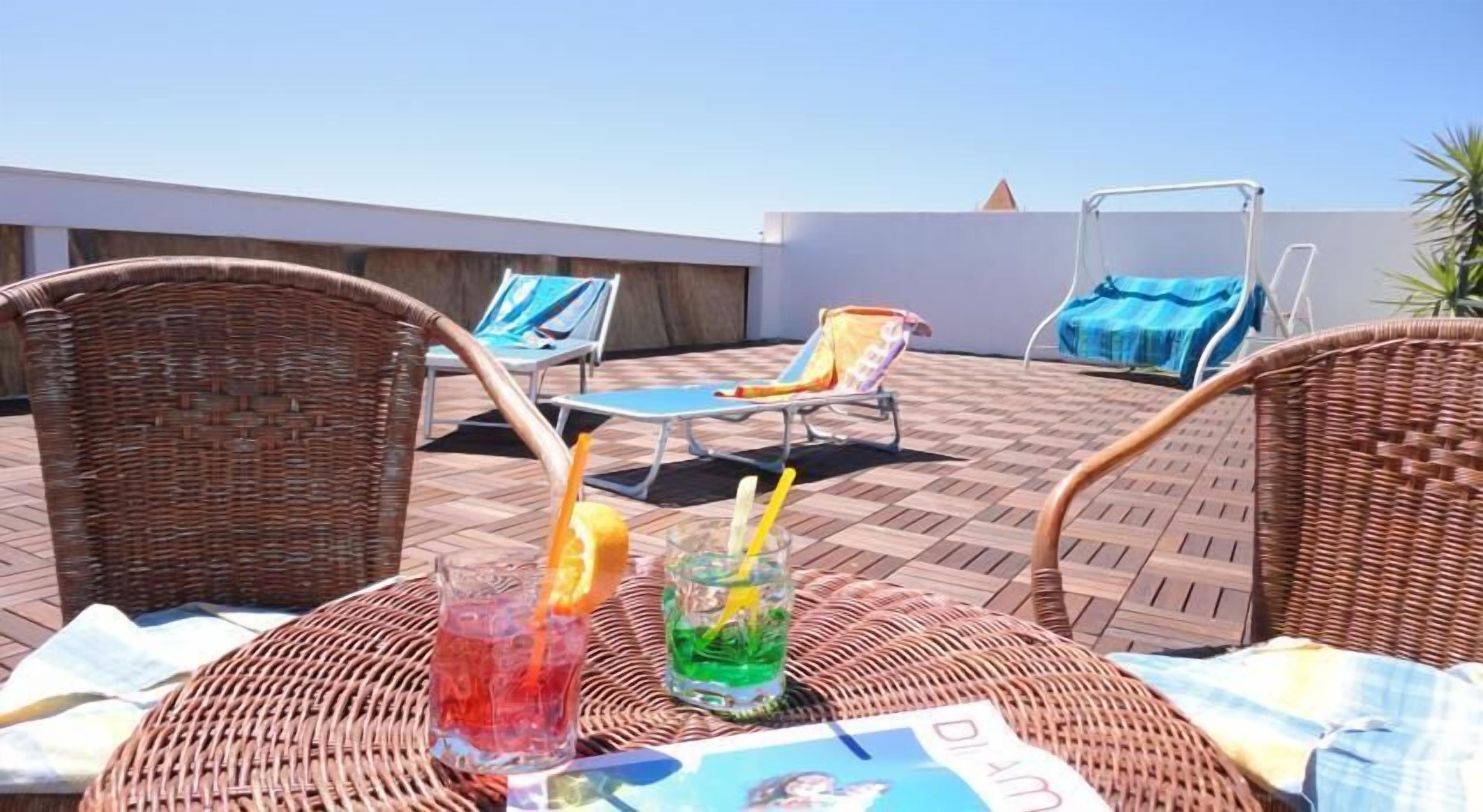 Una terraza en la azotea con sillas de mimbre, una mesa con bebidas y un área de piscina al fondo.