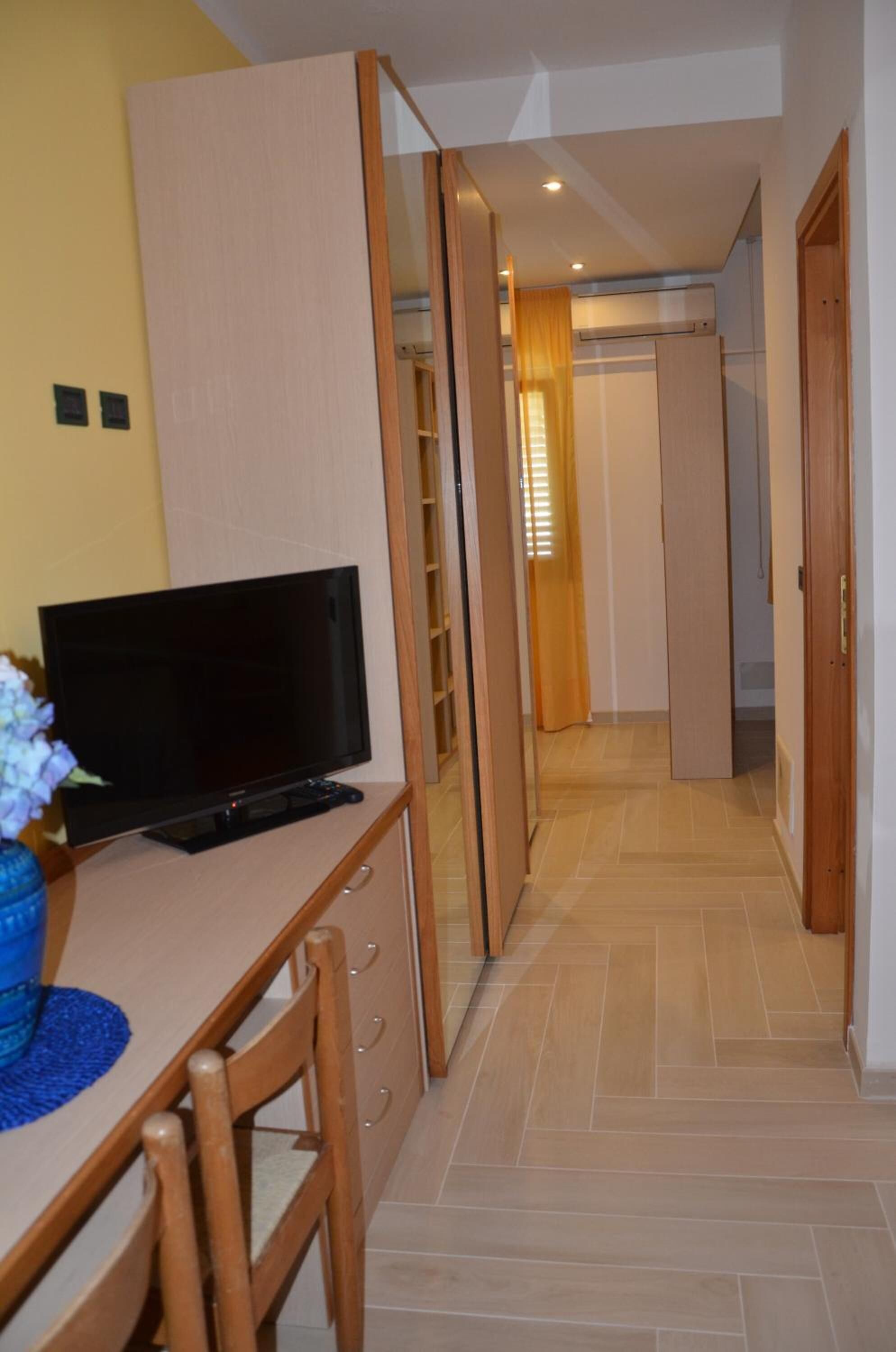 Une pièce avec un téléviseur posé sur un bureau en bois, une chaise et un vase bleu rempli de fleurs.