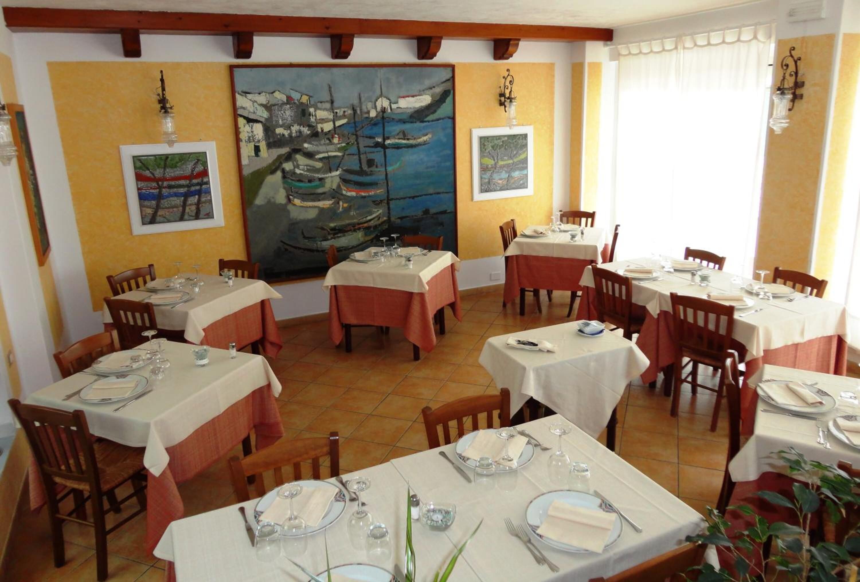 A dining area with multiple tables set for meals, wooden chairs, and artwork on the walls.