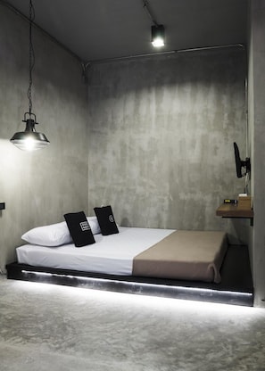 Ein schlicht eingerichtetes Schlafzimmer mit Bett, zwei Kissen, Nachttisch und Pendelleuchte.