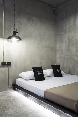A modern bedroom with a bed, a hanging light fixture, and a wall-mounted control panel.