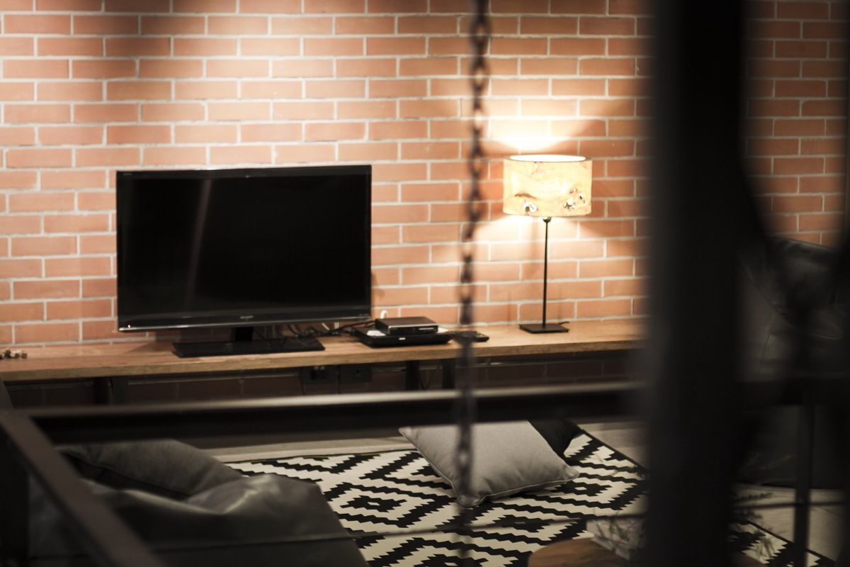 A modern living room with a brick wall, a flat-screen TV, a wooden console, and a patterned rug.