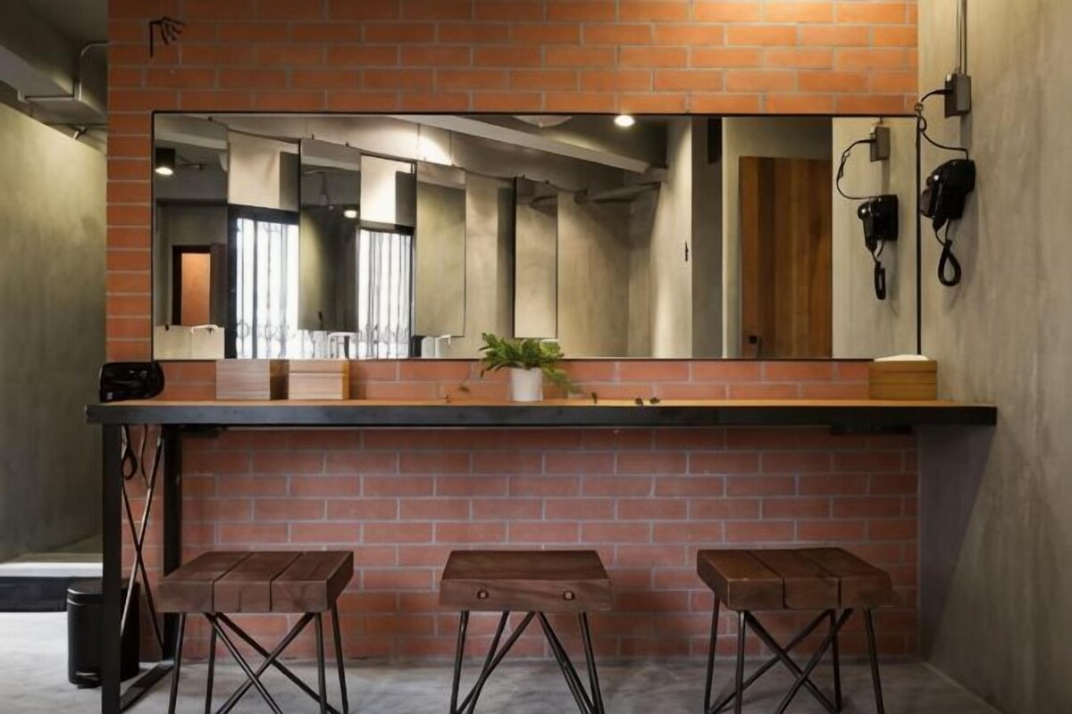 A restroom with a brick wall, a large mirror, and three wooden stools.
