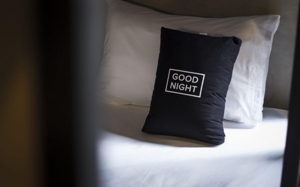 Un llit amb un coixí que té escrit "BONA NIT".