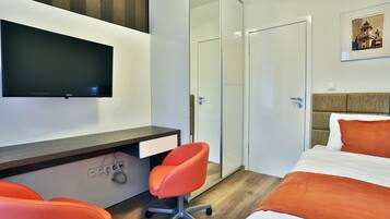 Una habitación de hotel moderna con una cama, un escritorio con silla, un televisor y un armario.