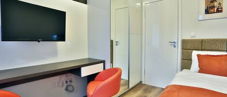 A modern hotel room with a bed, a desk with a chair, a TV, and a wardrobe.