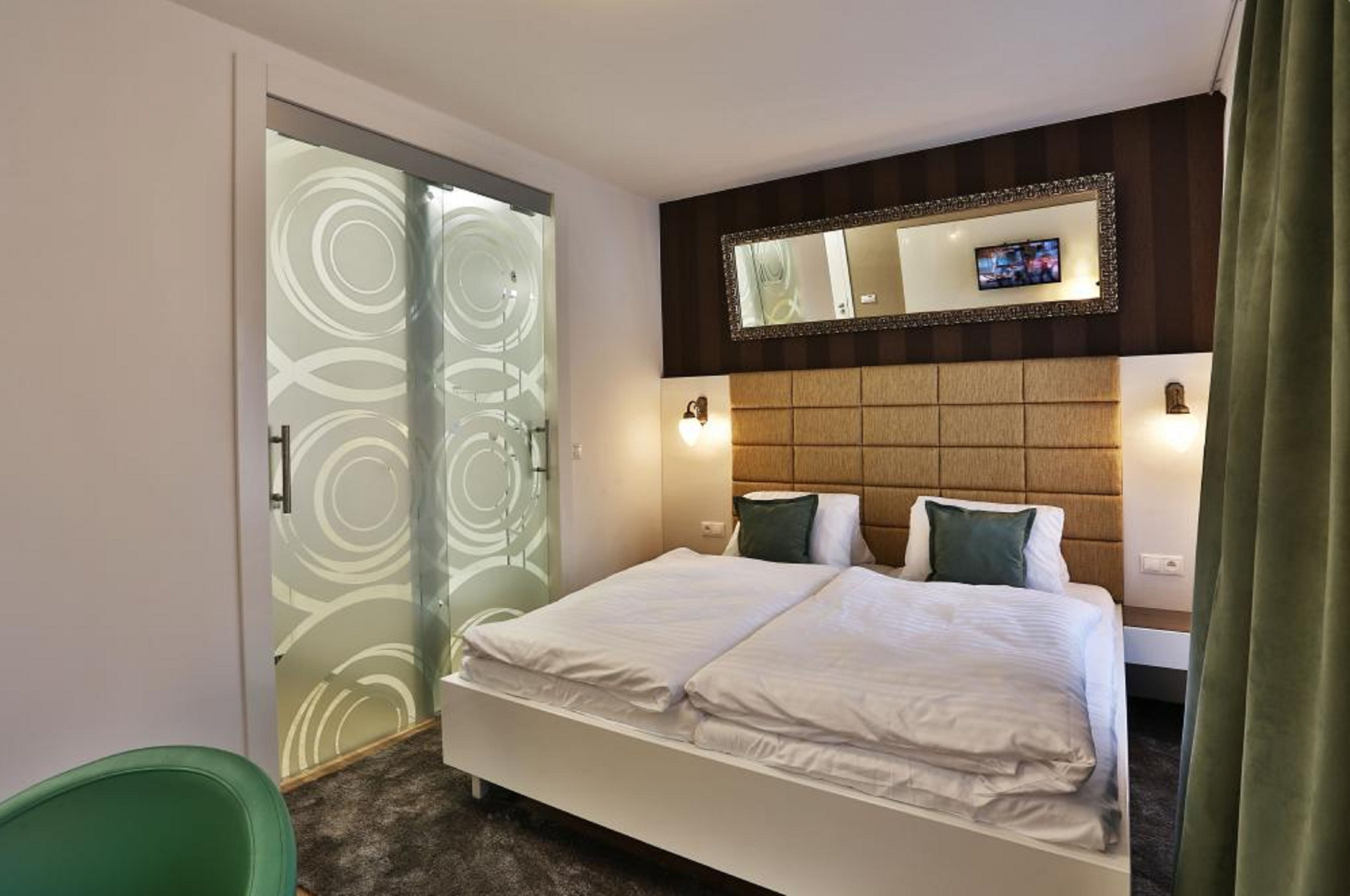 A hotel room with a bed, a television above the headboard, and a mirror with a decorative frame.