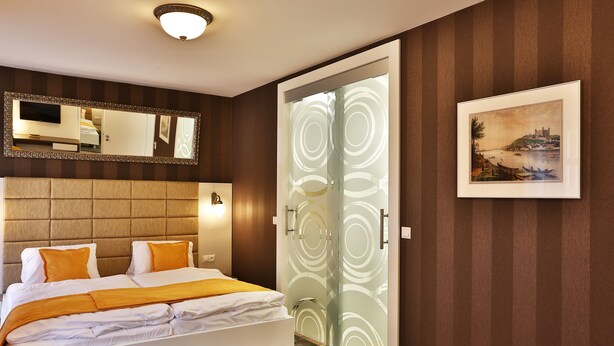 Una habitación de hotel moderna con una cama, un espejo grande, un cuadro enmarcado y una puerta de cristal con un diseño circular.