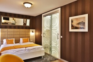 A modern hotel room with a bed, a large mirror, a framed picture, and a glass door with a circular pattern.