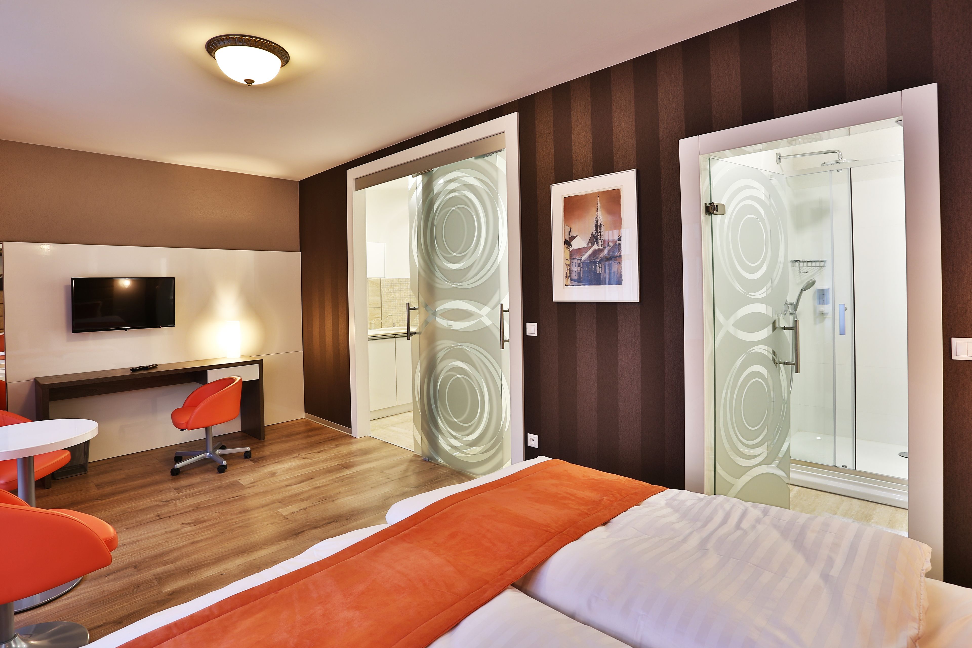 Hotellihuone, jossa on sänky, työpöytä tuolilla, televisio ja suihkutila.